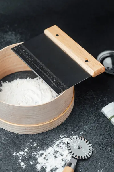 Un, karanlık bir mutfak yüzeyinde süzgeç ve kazıyıcı ile hazırlanıyor..