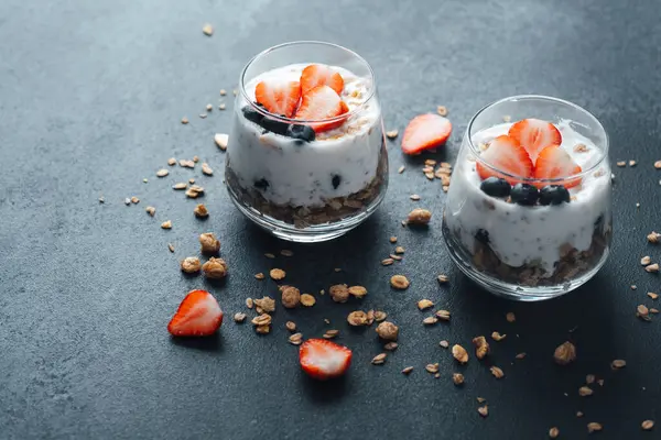 Yoğurtlu granola parfe, koyu arkaplanda çilek ve yabanmersini.