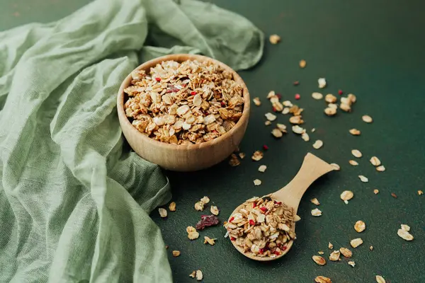 Tahta kase ve yeşil tekstil arka planında bir kepçe granola.