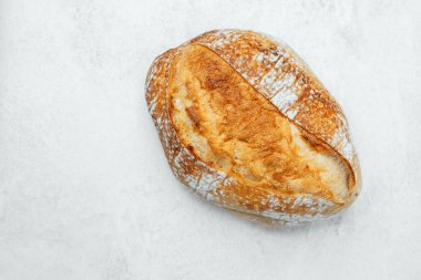 Kırsal bir ekmek somunu temiz bir yüzeye uzanır ve altın kabuğunu sergiler..