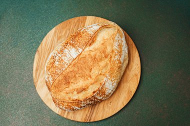 İçerideki ahşap kesme tahtasının üzerinde duran altın sarısı ekşi ekmek..