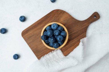 Olgun yaban mersiniyle dolu ahşap bir kase kesme tahtasının üzerinde duruyor..