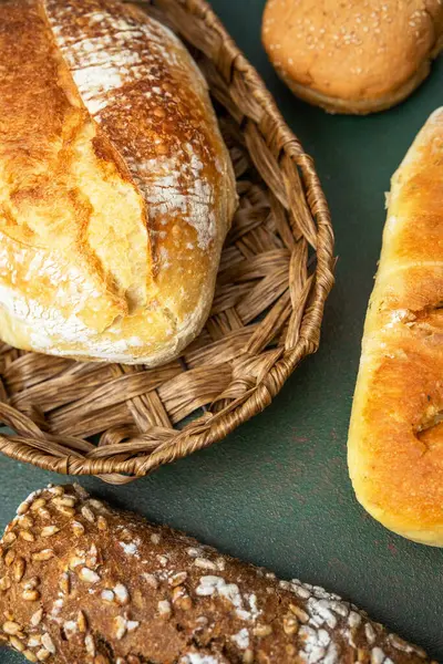 Yeşilin üzerinde dokuma sepetine yerleştirilmiş çeşitli taze ekmek türleri..