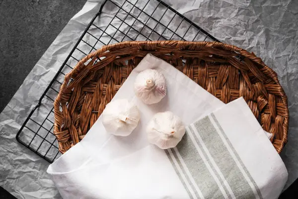 Hasır sepetin içindeki beyaz bir bezin üzerinde üç karanfil taze sarımsak dinleniyor..