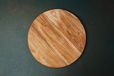 Doğal bir tahta kesme tahtası kullanıma hazır, karanlık bir mutfak yüzeyinde duruyor..