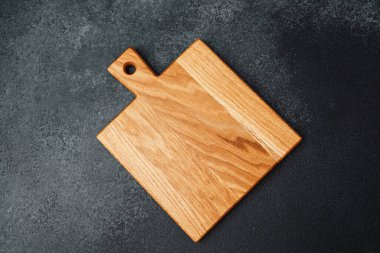 Eşsiz şekilli kahverengi bir tahta kesme tahtası karanlık bir yüzeye dayanır..