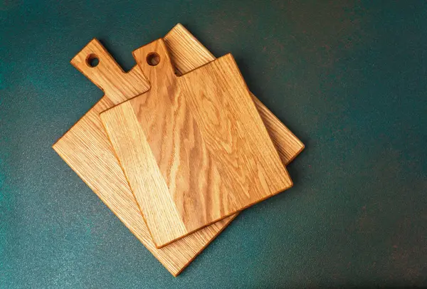 Farklı boyutlarda üç tahta kesme tahtası karanlık bir yüzeyde duruyor..