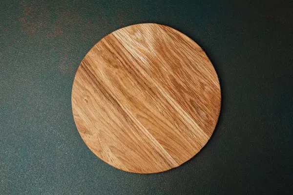 Doğal bir tahta kesme tahtası kullanıma hazır, karanlık bir mutfak yüzeyinde duruyor..