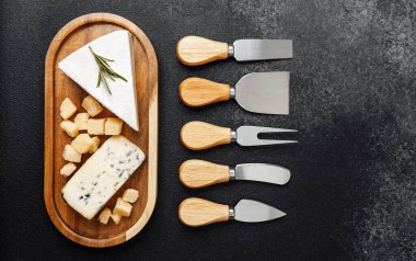 Tahta tepside çeşitli peynir bıçaklarıyla birlikte bir peynir seçimi..