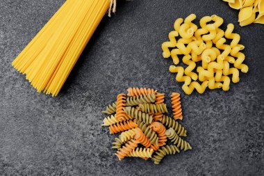 Yontulmuş bir yüzey üzerinde canlı renklerle çeşitli ham makarna şekilleri.