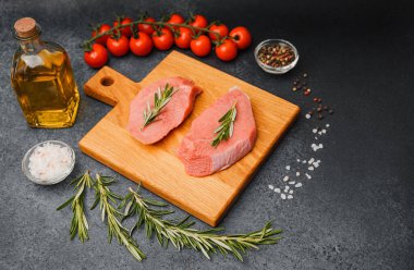 Kesme tahtasında biberiyeli çiğ biftek. Etrafı kiraz domatesleri, yağ tuzu ve biberle çevrili.