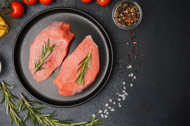 Siyah seramik tabakta çiğ biftek, biberiye, kiraz, domates, tuz ve biber.