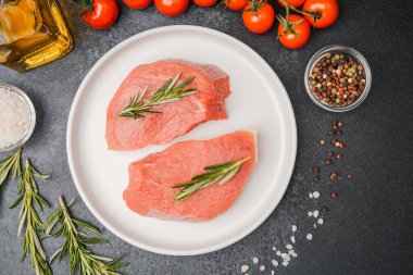 Beyaz seramik tabakta çiğ biftek, domates, tuz ve biber.