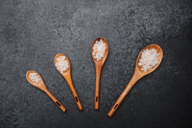 Siyah zemin üzerinde pembe himalaya tuzu olan tahta kaşıklar.