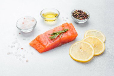 Bitkilerle süslenmiş somon filetosu ve yanında limon dilimleri ve baharatlar..