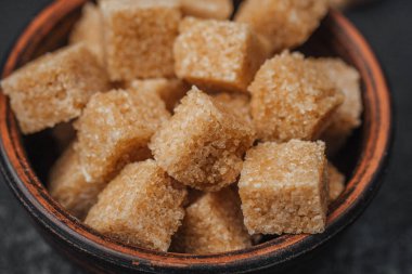 Kahverengi şeker küpleri, kristal dokularını ve renklerini vurgulayan, kırsal bir kaseyi doldurur..