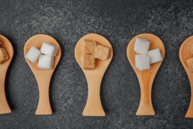 Koyu arkaplanda tahta kaşıklarla sıralanmış farklı şeker küpleri..