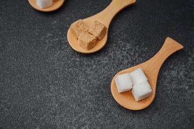 Koyu arkaplan üzerinde tahta kaşıklarda gösterilen çeşitli şeker küpleri.