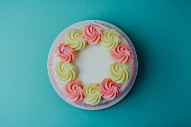 Üzerinde pembe ve sarı krema olan yuvarlak bir pasta mavi bir yüzeyde duruyor..