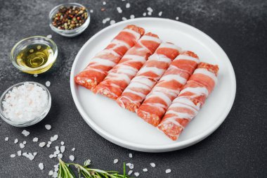 Çiğ domuz pastırması beyaz tabağa sarılmış, baharatlı ve otlu.