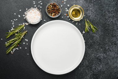 Siyah taş zemin üzerinde bitkiler ve baharatlar olan boş beyaz tabak