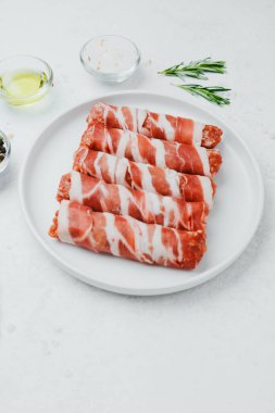 Jambona sarılmış sosis, beyaz tabakta otlar ve yağla birlikte.