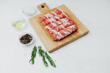 Domuz pastırmasına sarılı sosisli börekler, ahşap tahtada otlarla.