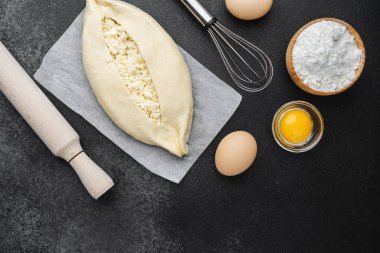 Süzme peynirli çiğ khachapuri ve siyah arka plandaki malzemeler.