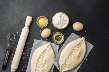 Malzemelerin üst görüntüsü ve iki pişmemiş khachapuri un kaplı siyah masa üzerinde