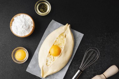 Parşömen üzerinde peynir ve sarısı olan Khachapuri ve koyu mutfak masası.