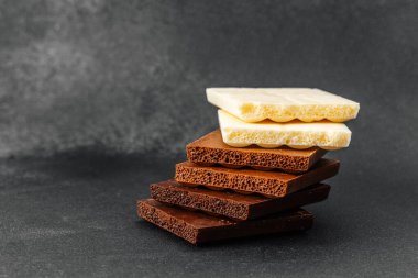 Siyah zemin üzerinde beyaz, süt ve koyu aromalı çeşitli çikolata parçaları yığını