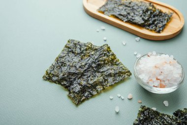 Yeşil arka planda cam kasede tuz bulunan kavrulmuş yosun çerezi.