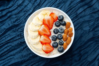 Koyu mavi tekstil arka planında meyveler ve bademlerle yulaf ezmesi kasesi
