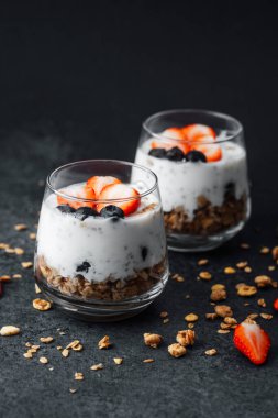 Yoğurtlu granola parfe, koyu arkaplanda çilek ve yabanmersini.