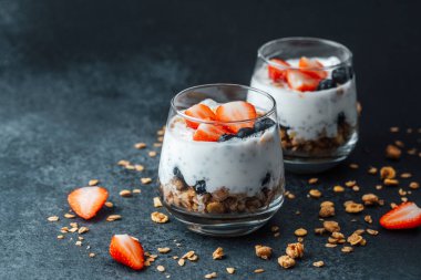Yoğurtlu granola parfe, koyu arkaplanda çilek ve yabanmersini.