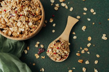 Tahta kase ve yeşil tekstil arka planında bir kepçe granola.