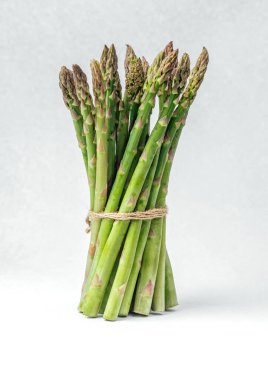 Tarafsız bir arkaplanda sicimle bağlanmış bir avuç taze kuşkonmaz..