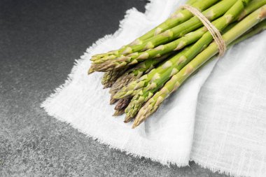 Yeşil kuşkonmaz mızrakları toplandı ve bağlandı, dokulu kumaştan bir arkaplanda dinleniyorlar..