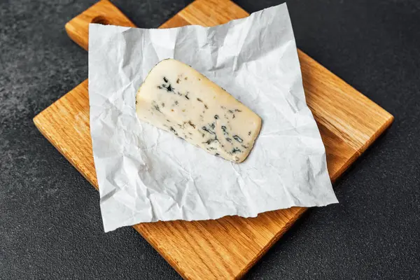 Parşömene sarılı mavi peynir Tahtaya oturmuş tadılmaya hazır.