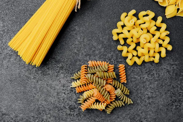 Yontulmuş bir yüzey üzerinde canlı renklerle çeşitli ham makarna şekilleri.