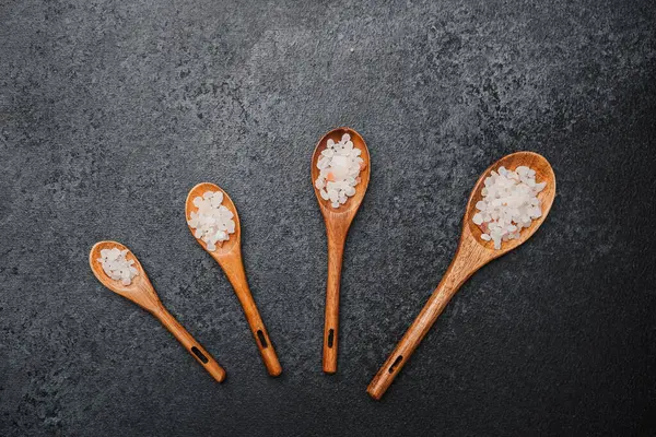 Siyah zemin üzerinde pembe himalaya tuzu olan tahta kaşıklar.