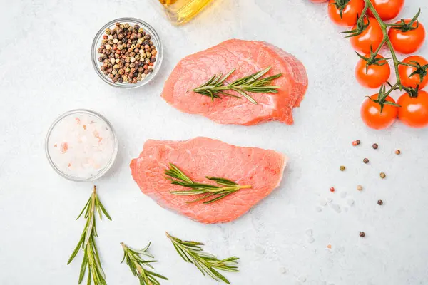 Beyaz arka planda baharatlı dana bifteği ve bitkilerin üst görüntüsü, yakın plan yağ ve biber dahil.