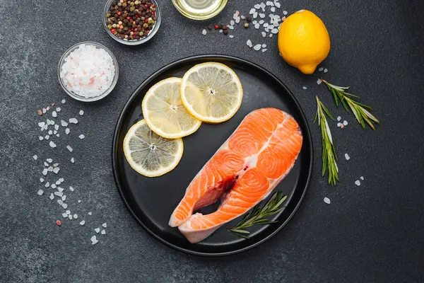 Limon dilimleri ve baharat için bitkilerle birlikte siyah tabakta taze somon filetosu..
