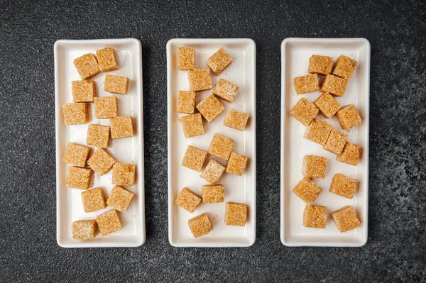 Kahverengi şeker küpleri sunum için üç beyaz tabakta güzelce düzenlenir..