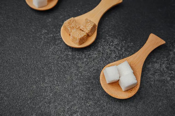 Koyu arkaplan üzerinde tahta kaşıklarda gösterilen çeşitli şeker küpleri.