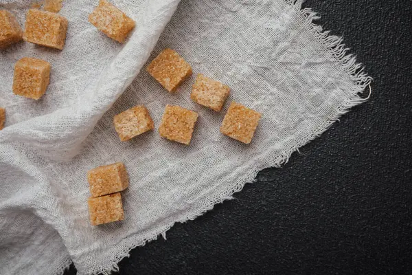 Kahverengi şeker küpleri beyaz bir bez peçeteye saçılmış, kırsal bir görünüm yaratıyor..