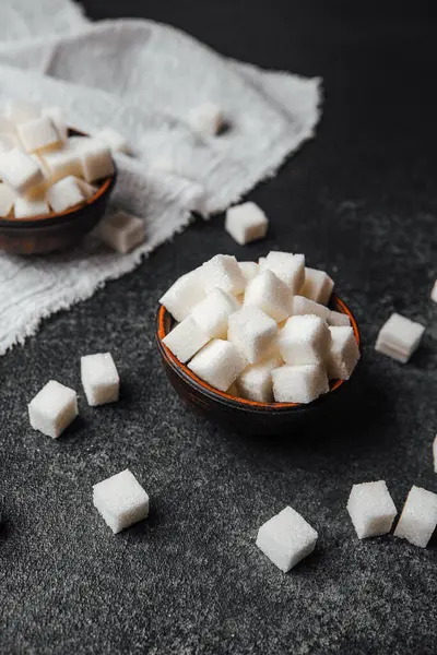 Küçük beyaz şeker küpleri, karanlık bir yüzeydeki kırsal kaselerde sanatsal olarak düzenlenir..