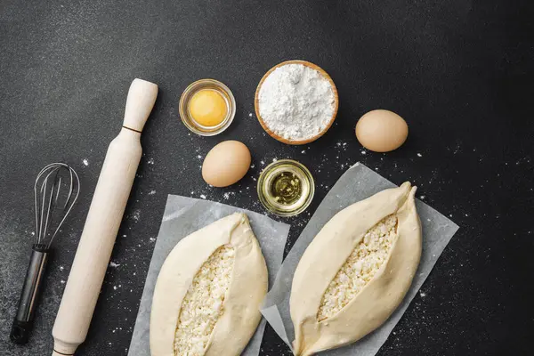 Malzemelerin üst görüntüsü ve iki pişmemiş khachapuri un kaplı siyah masa üzerinde