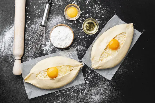 Un kaplı yüzeyinde yumurta sarısı olan iki çiğ khachapuri.