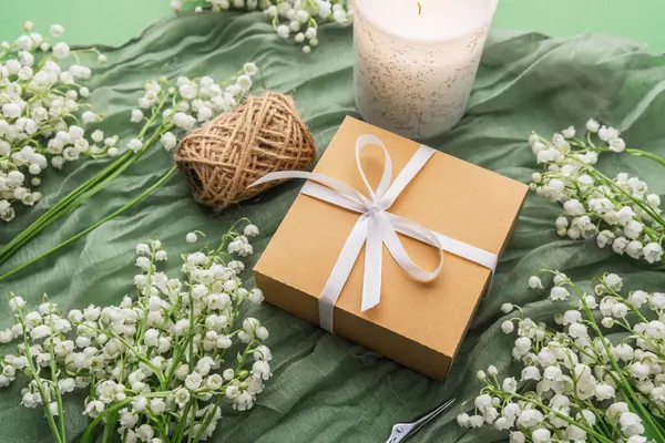 Yeşil kumaş arka planında hediye kutusu olan sicim, mum ve çiçekler.